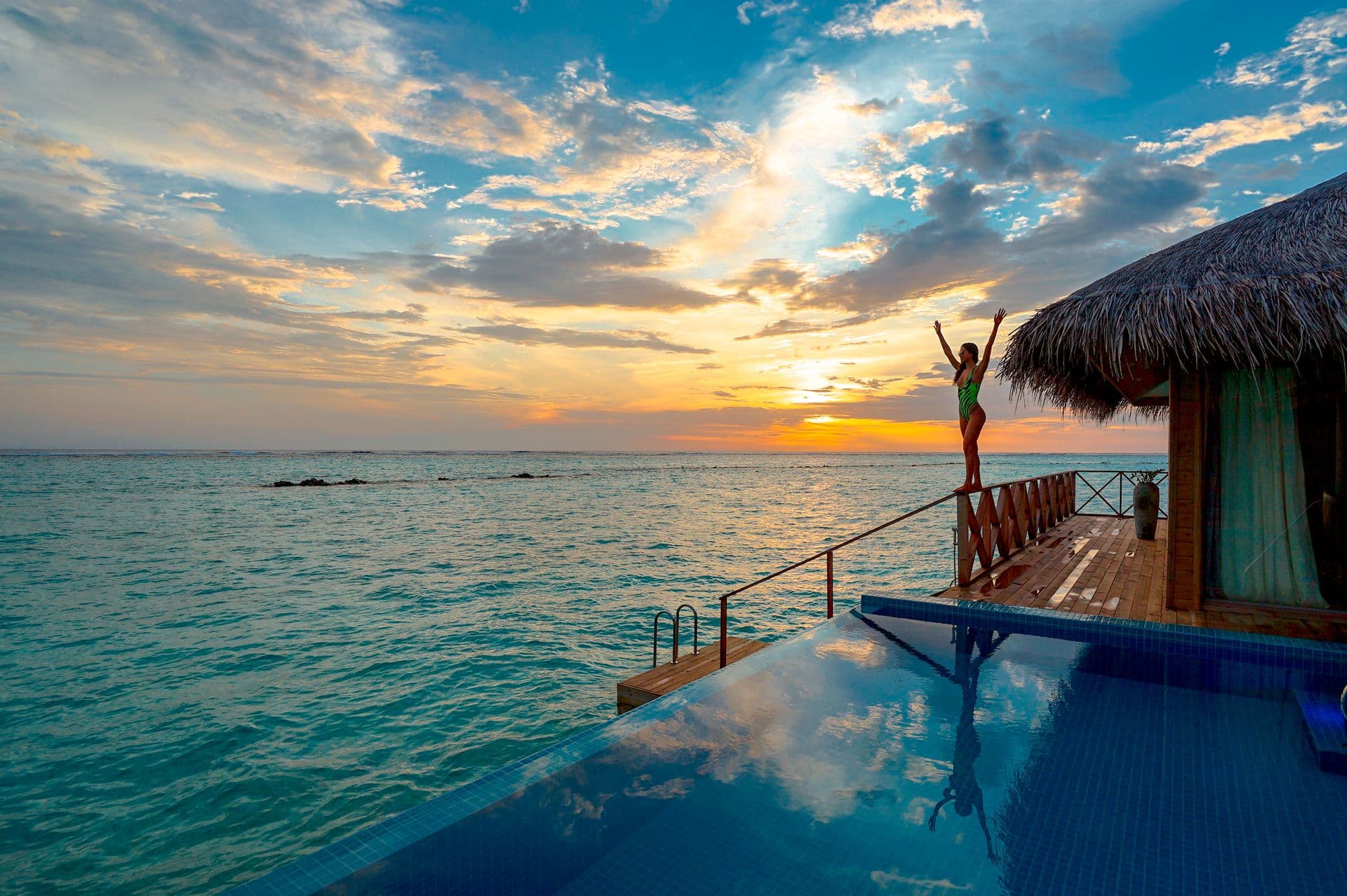 Traveler greeting the sunset from an infinity pool over the Indian Ocean